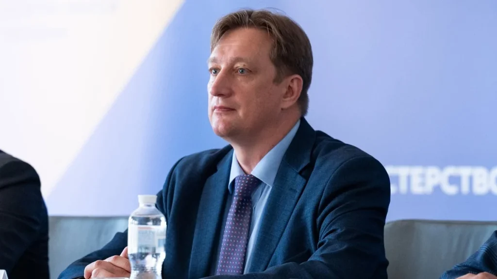 Андрій Бутенко в синьому костюмі сидить на офіційному заході
