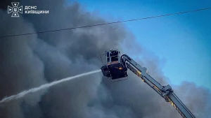 Рятувальник у кошику автодрабини гасить пожежу струменем води серед густого диму