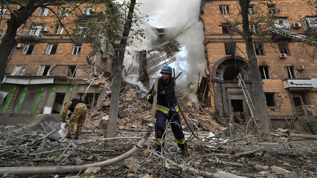 Пожежник з шлангом серед руїн зруйнованої будівлі з димом